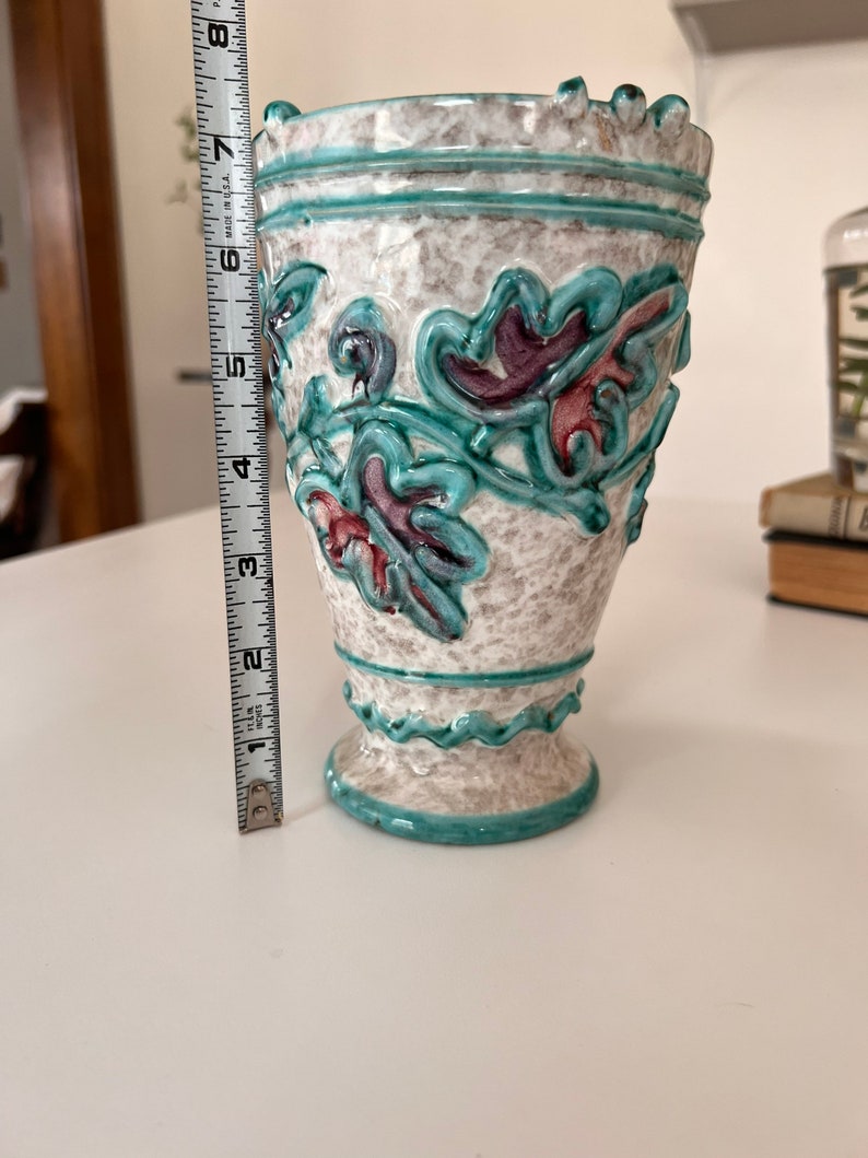 May include: A white ceramic vase with a turquoise glaze and raised floral design. The vase has a scalloped rim and base.