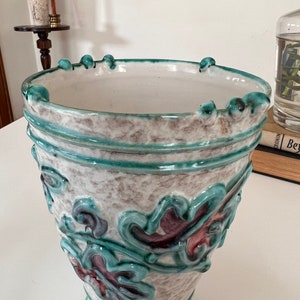 May include: A white ceramic vase with a green and purple floral design. The vase has a wide mouth and a narrow base.