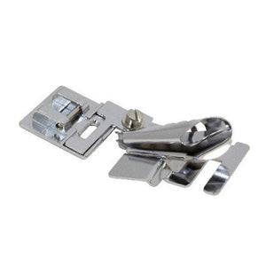 May include: Silver sewing machine foot attachment for rolled hems. The foot has a metal guide and a screw to adjust the height.