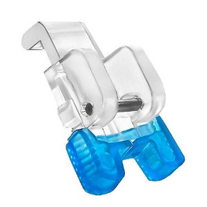 May include: A clear plastic sewing machine foot with a blue plastic attachment. The foot has a small metal pin and a clear plastic lever.