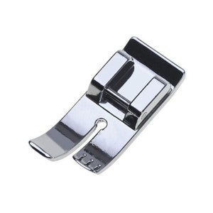 May include: A silver sewing machine foot with a small hole in the center and a curved edge.