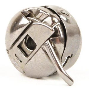 May include: A silver bobbin winder for a sewing machine. The winder has a metal arm and a round base.