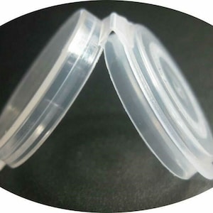 May include: Two clear, plastic, circular lids are slightly ajar, revealing their interior design. The lids are made of a translucent material, and the image is set against a dark background. The lids appear to be for a container.