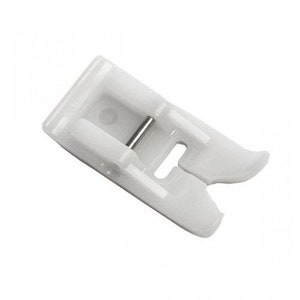 May include: A white sewing machine foot with a silver metal pin. The foot has a rectangular shape with a curved front and a slot for the needle. It is designed to help guide fabric evenly through the machine.