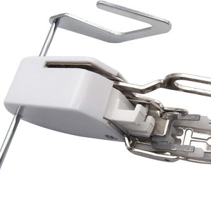 May include: A white and silver sewing machine foot with a metal bar and a U-shaped attachment. The foot has a complex design with multiple parts and is designed to attach to a sewing machine.