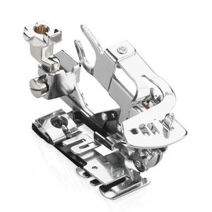 May include: A silver sewing machine foot attachment with a metal screw and a small metal lever. The foot is designed for sewing rolled hems.