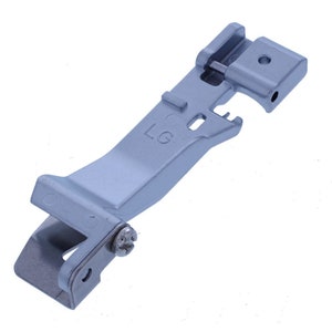 May include: A silver-colored sewing machine foot with a screw and the letters "LG" printed on it.