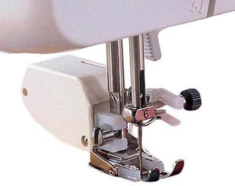May include: Close-up of a white sewing machine foot with a silver needle and a white plastic bobbin case. The foot is labeled with the number "6".