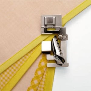 May include: A silver sewing machine foot attachment for creating a rolled hem. The foot is attached to a sewing machine and is used to create a neat, professional-looking rolled hem on fabric.