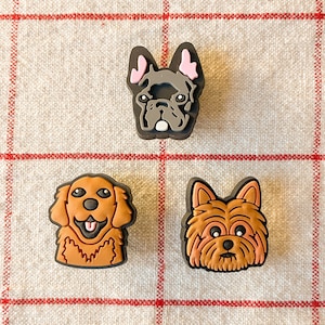 May include: Three dog face charms, a brown and black French Bulldog, a brown Golden Retriever, and a brown Yorkshire Terrier.