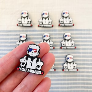 May include: A white cartoon figure wearing sunglasses and a red, white, and blue American flag bandana. The figure is giving the middle finger with both hands and the text "YOU MISSED" is below the figure.