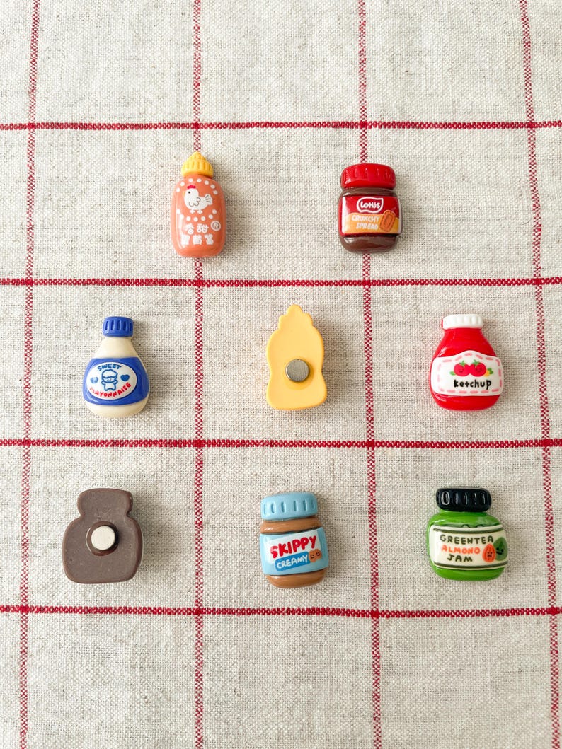 May include: A set of nine miniature food jar magnets, including ketchup, peanut butter, jam, and more. The magnets are colorful and feature cartoon-like illustrations.