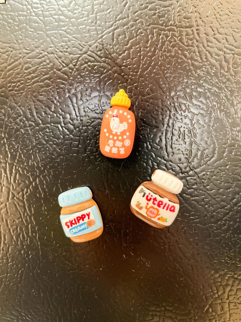 May include: Three miniature food jar magnets. A red and orange jar with a white chicken and the text "香辣鸡" in Chinese characters. A blue and brown jar with the text "SKIPPY CREAMY" in white. A brown jar with the text "NUTELLA" in white.