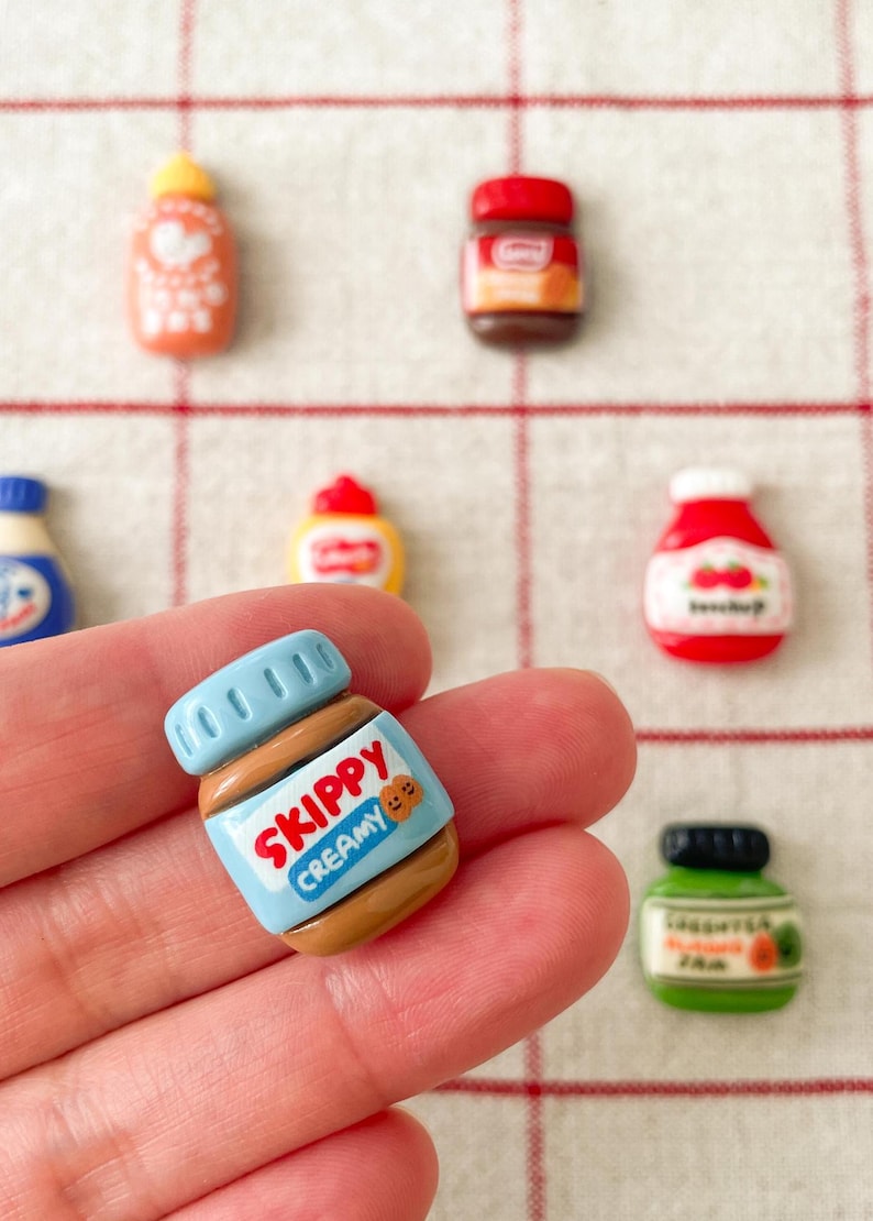 May include: A miniature plastic jar of Skippy Creamy peanut butter. The jar is blue and brown with a red label that says "Skippy Creamy".