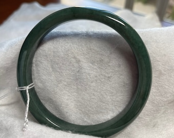 May include: A dark green jade bangle bracelet. The bracelet is smooth and polished.