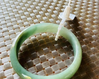 May include: A green jade bangle bracelet with a white tag attached.