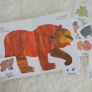 May include: A children's book with a brown bear on the cover. The book has a flap that lifts to reveal a smaller brown bear. The text on the cover reads "Brown Bear, Brown Bear, What do you see?" and "I see a red bird looking at me."