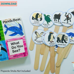 May include: An educational set for children, comprising a book titled "What Do You See?" and animal flashcards on wooden sticks. The flashcards illustrate animals such as pandas, turtles, and penguins. The book cover displays a panda and a blue sea creature.