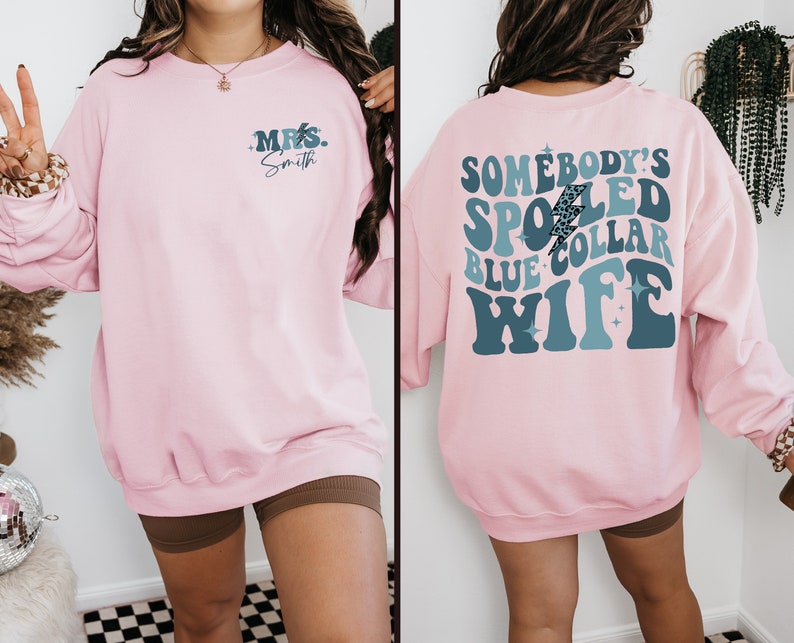 May include: Pink sweatshirt with a blue and white graphic on the back that says "Somebody's Spoiled Blue Collar Wife" and a smaller blue graphic on the front that says "Mrs. Smith".