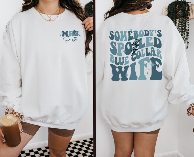 May include: White sweatshirt with blue and white text that says "Somebody's Spoiled Blue Collar Wife" with a lightning bolt graphic. The front of the sweatshirt has the text "Mrs. Smith" in blue.