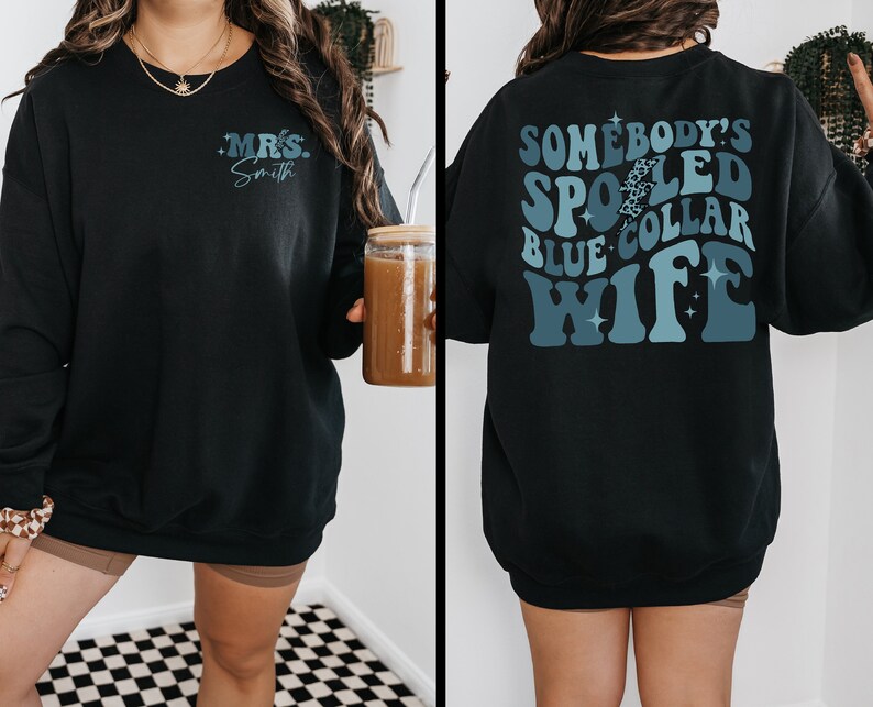 May include: Black sweatshirt with a blue and white graphic that says "Somebody's Spoiled Blue Collar Wife" on the back and "Mrs. Smith" on the front.