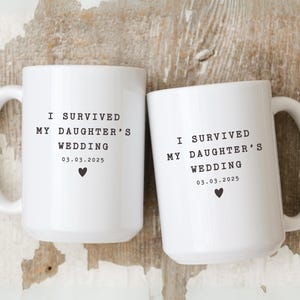 May include: Two white ceramic mugs with black text that reads "I survived my daughter's wedding 03.03.2025" and a small black heart.