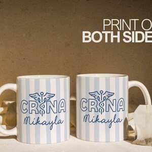 Pu&ograve; includere: Due tazze in ceramica bianca con strisce verticali blu e bianche. Ogni tazza presenta la scritta "CRNA Mikayla" in blu, insieme a un simbolo di caduceo. Le parole "PRINT ON BOTH SIDES" sono in bianco.