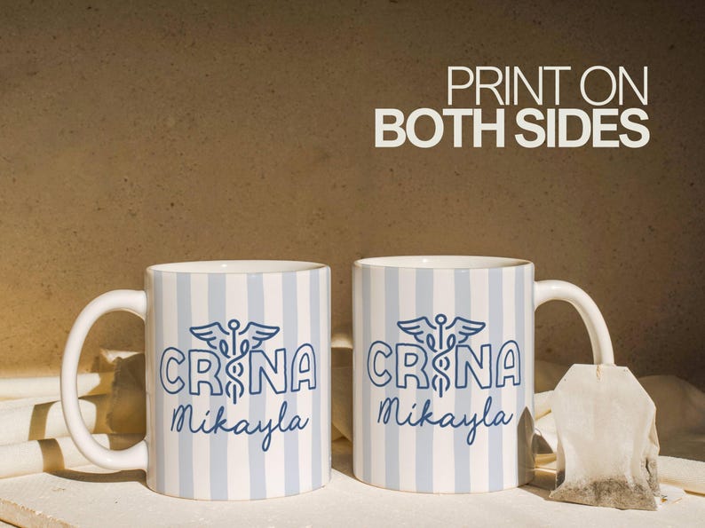 Pu&ograve; includere: Due tazze in ceramica bianca con strisce verticali blu e bianche. Ogni tazza presenta la scritta "CRNA Mikayla" in blu, insieme a un simbolo di caduceo. Le parole "PRINT ON BOTH SIDES" sono in bianco.