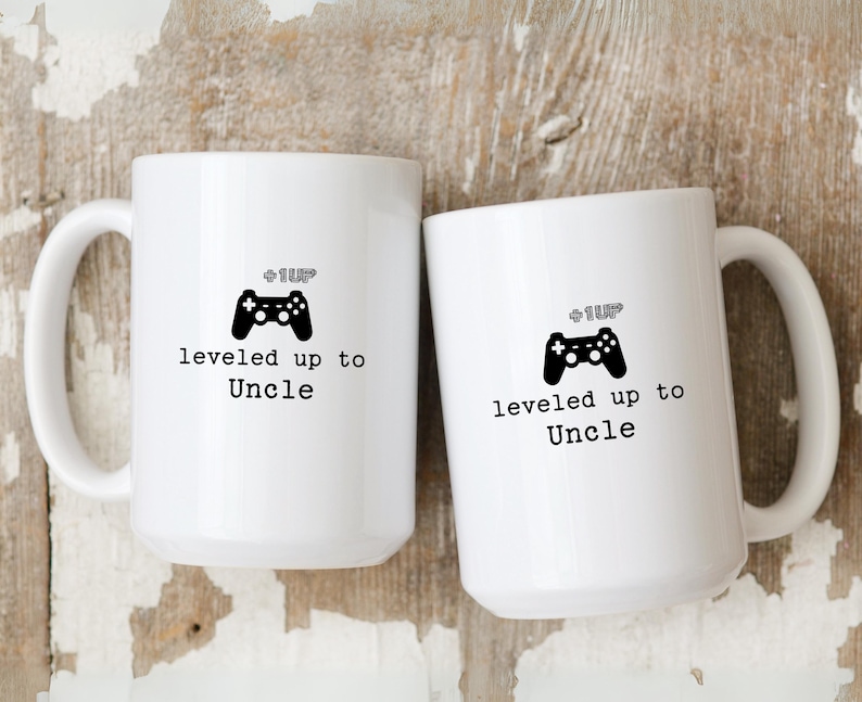 May include: Two white ceramic mugs with black handles. The mugs have a black video game controller graphic and the text "Level Up to Uncle".