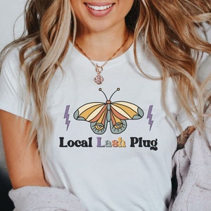 May include: White t-shirt with a colorful butterfly graphic and the text "Local Lash Plug".