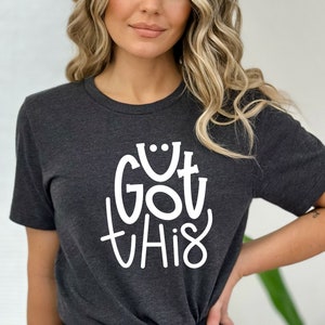 May include: A dark gray t-shirt with a white graphic that says "GOT THIS" in a playful, handwritten style.