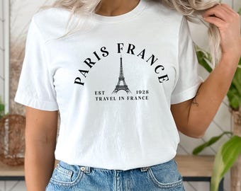 May include: White t-shirt with a black graphic design featuring the Eiffel Tower and the text "Paris France Est 1928 Travel in France".