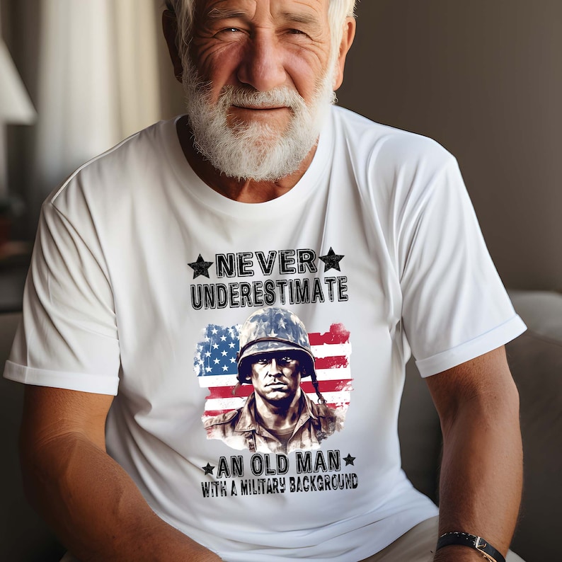 May include: White t-shirt with a graphic of a soldier in front of an American flag. The text on the shirt reads "Never underestimate an old man with a military background."