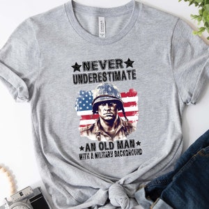 May include: Gray t-shirt with a graphic of a soldier in front of an American flag. The text reads "Never underestimate an old man with a military background."