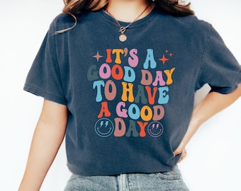 May include: A navy blue t-shirt with a colorful graphic that reads "It's a good day to have a good day". The graphic features a retro font style and smiley faces with lightning bolts.