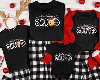 May include: A set of four black t-shirts with a Christmas theme. The shirts feature the text "Christmas Squad" with a Disney character on each shirt. The shirts are on a red and black plaid background.
