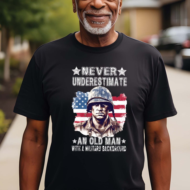 May include: Black t-shirt with a white graphic of a soldier in front of an American flag. The text "Never underestimate an old man with a military background" is printed on the shirt.