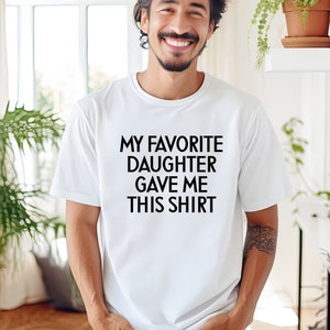 May include: White t-shirt with black text that reads "My favourite daughter gave me this shirt."