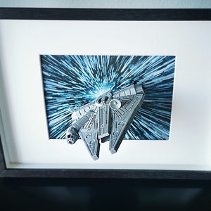 Könnte beinhalten: Ein gerahmtes Bild eines silbernen Raumschiffs, das durch einen blauen und weißen Lichtgeschwindigkeitseffekt fliegt.