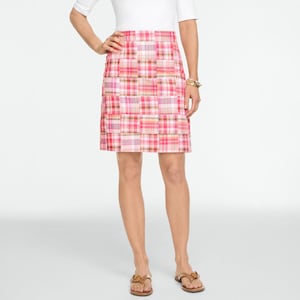 May include: A pink plaid skirt with a patchwork design. The skirt features a mix of pink, red, and white squares. The skirt is knee-length and has a straight silhouette. The person is wearing a white top and brown sandals.