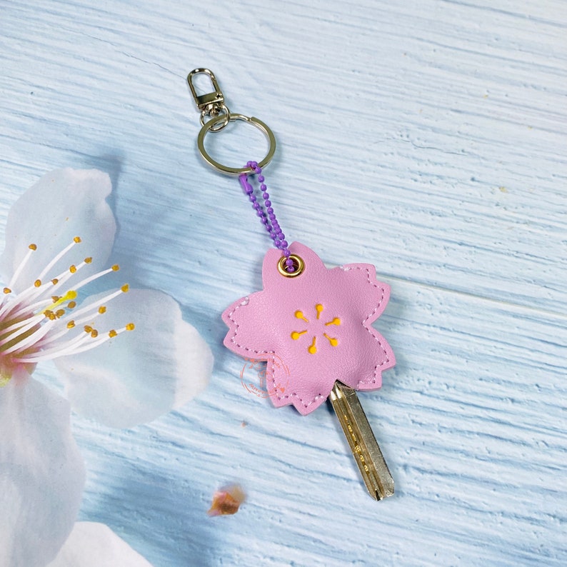 May include: A pink leather keychain shaped like a flower with a yellow center. The keychain has a silver ring and a purple chain.