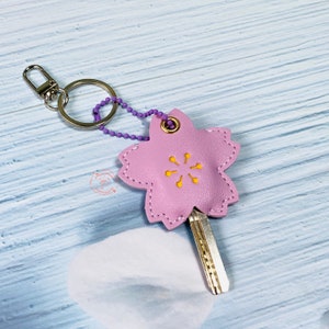 May include: A pink leather key chain shaped like a flower with a yellow center. The keychain has a silver key ring and a silver chain.