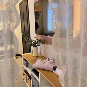 May include: A light wood entertainment center with open shelves and storage baskets. A lavender hoodie with the word "becoming" is on top. A black TV is mounted on the wall above the center.