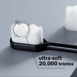 May include: Close-up of a black toothbrush with a white, ultra-soft brush head. The brush head has 20,000 bristles.