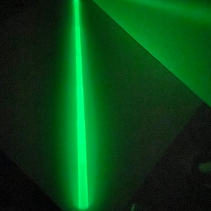 May include: A single, bright green glow stick on a dark surface.