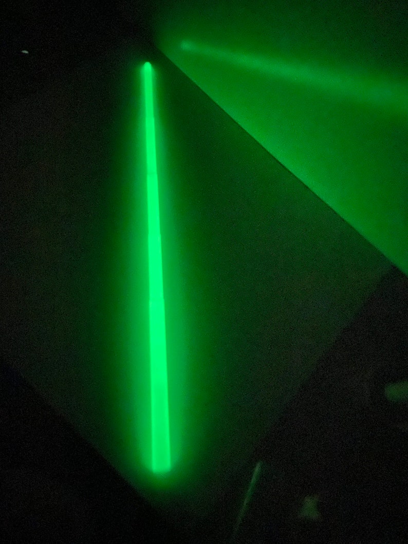 May include: A single, bright green glow stick on a dark surface.