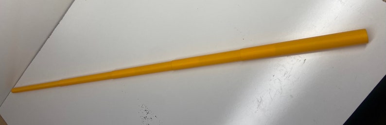 May include: A yellow telescopic pole, approximately 48 inches long, made of plastic. The pole is fully extended and appears to be made of two sections that slide together.