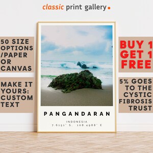 Può includere: Una stampa incorniciata raffigurante una scena costiera con spiaggia, onde e una roccia ricoperta di vegetazione verde. La stampa include il testo "Pangandaran, Indonesia" e le coordinate. La cornice è dorata e il testo "classic print gallery" è in alto.