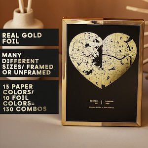 Puede incluir: Una impresión enmarcada con un mapa de lámina dorada en forma de corazón sobre un fondo negro. El marco dorado rodea la obra de arte. El texto en la impresión dice "Boston Me London You" y "Distance divides us, love unites us."