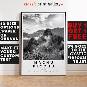 May include: Black and white framed print of Machu Picchu, Peru. The print includes the text "MACHU PICCHU" and coordinates. Additional text includes "50 SIZE OPTIONS / PAPER OR CANVAS" and "MAKE IT YOURS: CUSTOM TEXT". The print is displayed on a wooden floor.